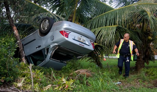 20081217_overturned-car-with-officer Officer Randy Aurello investigates an overturned vehicle in Hawaiian Paradise Park subdivision Wednesday morning. A witness said he saw the driver fleeing the scene on foot with the wheels still spinning on the upside-down vehicle. A fire department engine and medic unit also responded with the medic being called back due to the lack of a victim present.(Photo by Baron Sekiya/Hawaii247.com)