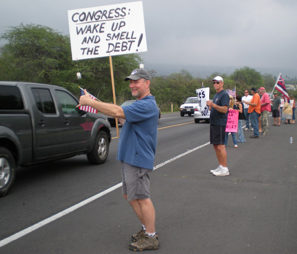 taxteaparty4 Scott Henderson, of Waikoloa, waves to drivers Wednesday in Kona during the Tax Day Tea Party. (Hawaii247.com photo by Karin Stanton)