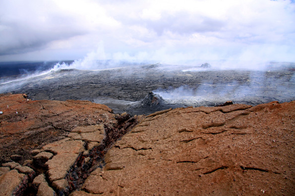 A view of Puʻu ʻŌʻō crater from the north, looking southeast. In the foreground, the crater rim has red hues due to oxidized cinder and spatter from the early days of Puʻu ʻŌʻō in the 1980s. In the center of the photograph, the black crater floor consists of lava flows erupted in the last several years, with several spatter cones built upon these flows. Near the left edge of the photograph, a small perched lava pond has been active in recent months. Photo courtesy of USGS/HVO