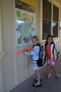 IMG_5942 After biking to school, 1st grader Sadie Blevins places the sticker she earned on the "Road to a Greener Planet" as classmate Nai'a Jones looks on.