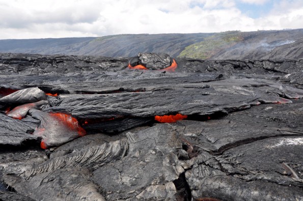 usgs-tumuli-pahoehoe The western branch of the coastal plain flow field is inflated and more active than the eastern branch. Here, a breakout from a tumuli feeds a ropey pahoehoe flow. The fume in the background on the pali marks the lava flow activity that is feeding the coastal breakouts. Photo courtesy of USGS/HVO