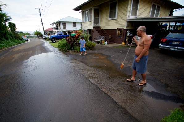20121128_papaikou-water-break 001 A resident downhill from the damaged pipe sweeps away mud and debris washing down the roadway. Photography by Baron Sekiya | Hawaii 24/7