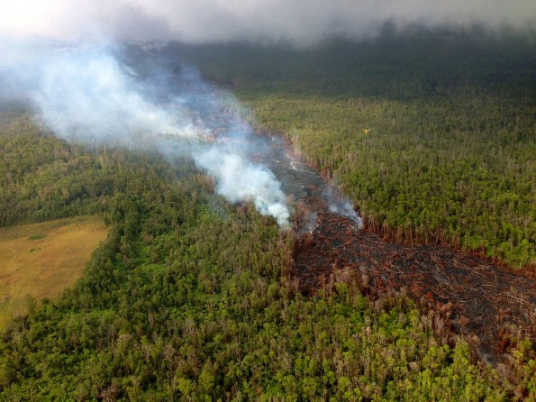 Smoke from burning vegetation marks the edges of small breakouts from the June 27th lava-tube system north of the abandoned geothermal well site (middle left). This was the lowermost breakout as of this morning, located approximately 12 km (7.5 mi) straight line distance from Puʻu ʻŌʻō. Smoke and steam from breakouts upslope are also visible in the distance. Note yellow-colored helicopter for scale (middle right). Photograph courtesy of Volcano Helicopters, taken before 11 am November 19, 2014.