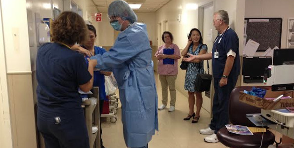 Dr. David Hefer dons personal protective equipment with help of ICU staff/buddies. In background from left to right: Lisa Downing, RN Infection Prevention Director, Dr. Sarah Park, State Epidemiologist, Hawaii DOH and Kevin Brunsen, RN, ICU nurse. (Photo courtesy of Kona Community Hospital)