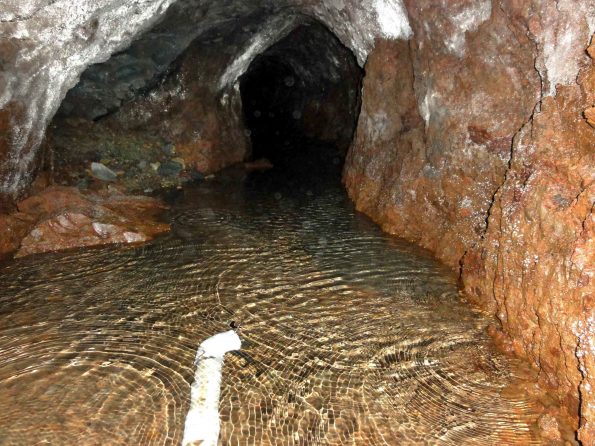 Interior of a water tunnel though ash layers in the Ka‘ū district. Water collects near the tunnel entrance and is transported by PVC pipe for agricultural use. USGS Photo.