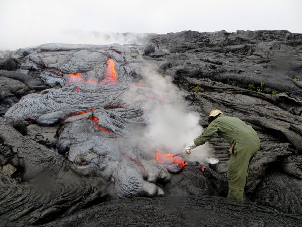A USGS Hawaiian Volcano Observatory geologist collects a sample of pāhoehoe lava on Kīlauea Volcano’s East Rift Zone. Steam rising from the flow resulted from heavy rain falling on the hot lava. Analyses of this and other samples provide information on the changing temperatures of Kīlauea lavas, which, in turn, reveal information about the volcano’s internal plumbing and magma transport processes. USGS photo by J. Babb