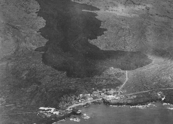 The dark-colored ‘a‘ā flow advancing toward the South Kona coastal village of Ho‘ōpūloa (foreground) on April 17, 1926, is a reminder of why Island of Hawaiʻi residents should be aware of the hazards posed by the volcanoes on which they live. This flow was fed by eruptive vents that opened high on Mauna Loa’s Southwest Rift Zone three days earlier. It was 1,500 feet wide and about 30 feet high in this aerial photo, but the ‘a‘ā flow continued to widen and thicken as it pushed through the village and reached the ocean on the morning of April 18. Photo courtesy of Army Air Corps, 11th Photo Section.