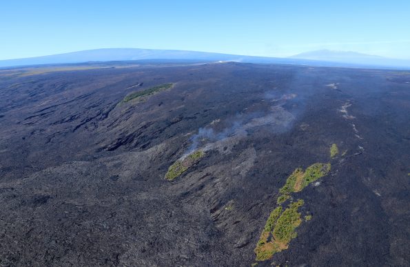Spectacular aerial view of Kīlauea Volcano’s East Rift Zone lava flows advancing over Pūlama pali in mid-December 2017. As surface lava flows moved through the center kipuka (forested area) on the pali, smoke rose from the burning vegetation. Gases emitted from Pu‘u ‘Ō‘ō, the source of the 61g lava flow, can be seen in the distance above the smoke from the burning kipuka. Mauna Loa (left) and Mauna Kea (right) are visible in the far distance. If you look carefully in front of Mauna Loa, you can see the gas plume rising above Halemaʻumaʻu at the summit of Kīlauea. Capturing both the summit and East Rift Zone eruptions in one photo is a rare sight! USGS photo by C. Parcheta.