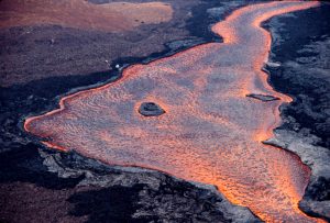 Mauna Loa tends to erupt large, fast-moving lava flows. About 36 hours after the 1984 eruption began on March 25, lava flowed downstream (toward bottom-right of photo) through this ‘a‘ā channel down rift from the main vent. For scale, note the USGS scientists at work on the left side of the 70-m- (77-yard-) wide lava channel. Photo courtesy USGS