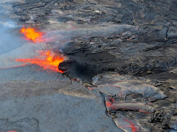 The summit lava lake level remained high throughout Wednesday, April 25, sending occasional overflows across the floor of Halema‘uma‘u. A spattering site (upper left) poured lava into a small overflow directed to the north. A passive overflow of the lava lake rim (bottom right) sent a more sluggish lava flow onto the floor of Halema‘uma‘u. Just left of center in this photo, a spattering source has constructed a spatter rampart on the lake margin. Photo taken Wednesday, April 25, 2018 courtesy of U.S. Geological Survey