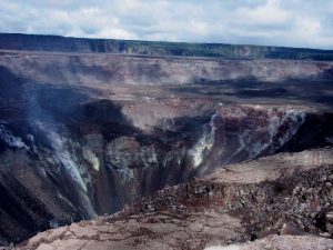 What is next for Kīlauea Volcano? This is a view of the summit area from the southwest, showing the collapsed area of Halema‘uma‘u and the adjacent caldera floor. A section of Crater Rim Drive preserved on a down-dropped block is visible at the far right. Volcanic gases rising from magma stored beneath the summit continue to escape to the surface, as they have for as long as Kīlauea has existed, resulting in deposits of sulfur on the crater walls. USGS Photo by Don Swanson.