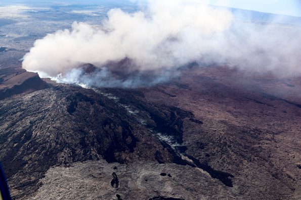 Puʻu ʻŌʻō on May 3, 2018, as viewed from the helicopter overflight. The crater floor is collapsed, and a thin plume escapes from the gaping crater. The west flank cracked on April 30th around 2:30 pm HST, and minor amounts of lava oozed out of the crack (line of steaming features) just before the plumbing system catastrophically failed.